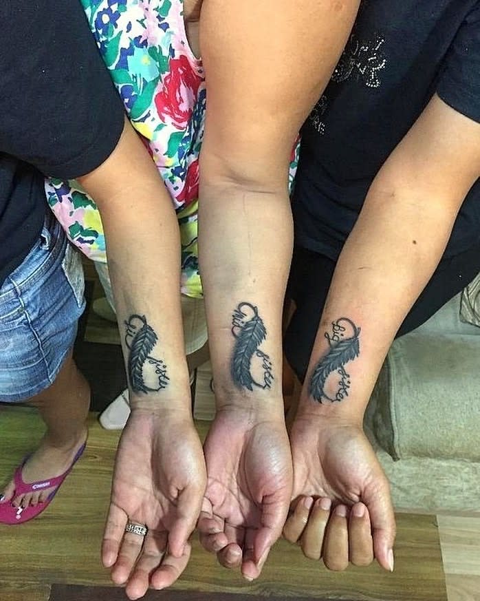 Matching feather tattoos with 'big sister' and 'little sister' in cursive script, symbolizing a close sisterly bond